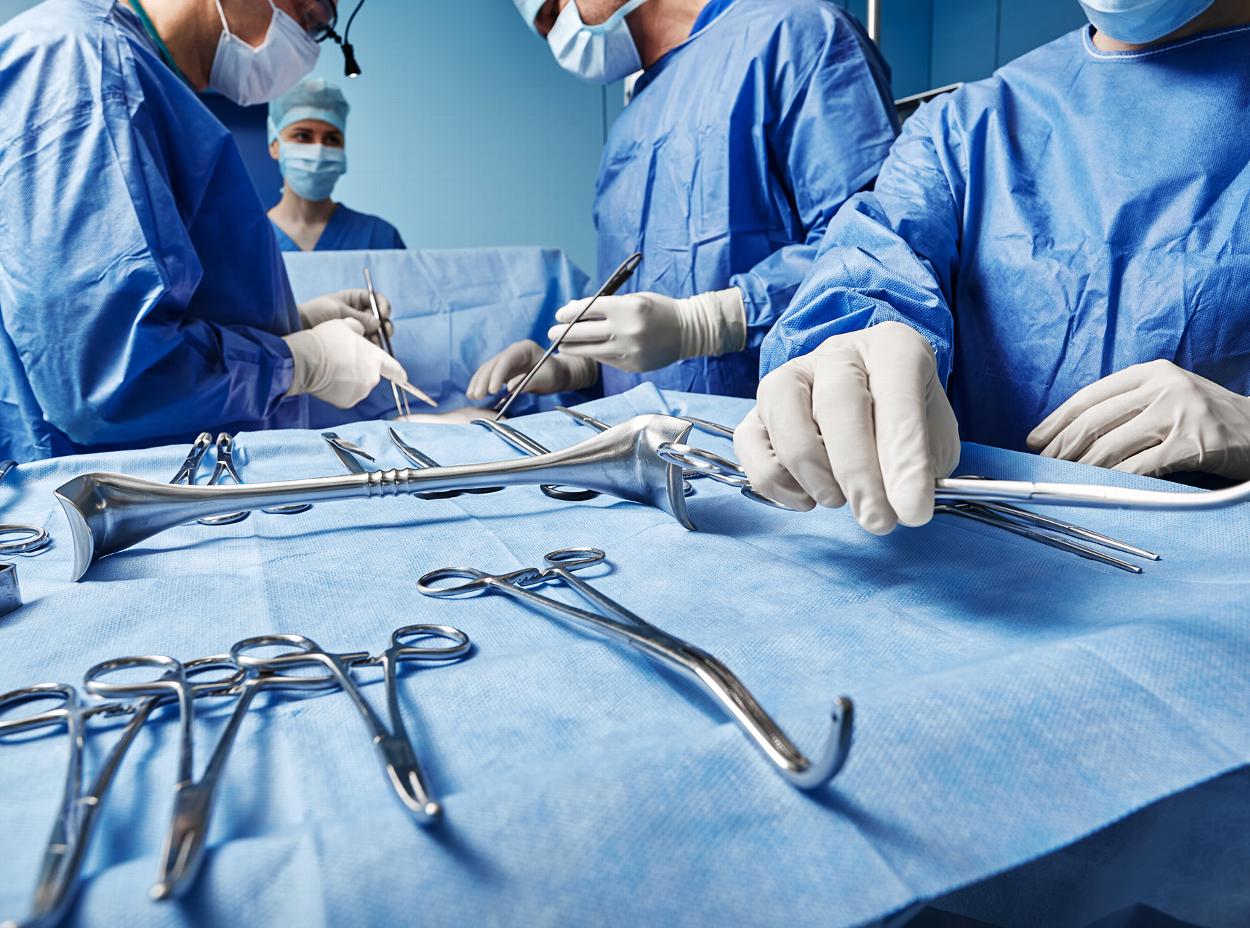 a team of assistants with a consultant in blue scrubs performing a surgery with steel surgical tools 