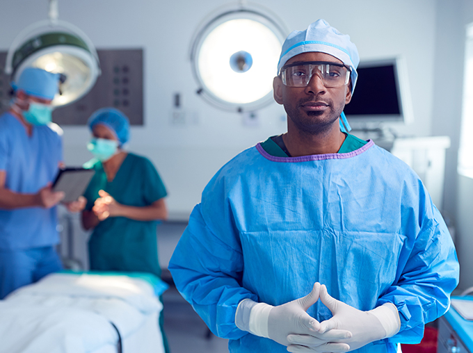 a consultant in blue theatre scrubs with two assistants in the background of an operating theatre