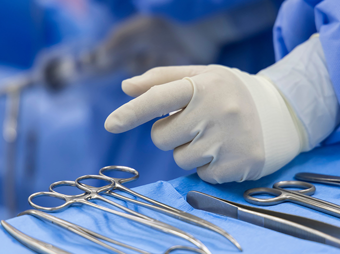 a person wearing a white latex glove with his hand near some surgical equipment on a blue clothed surface