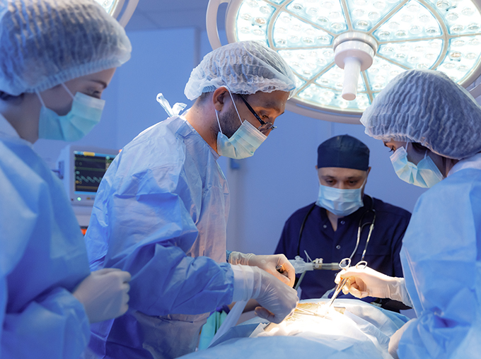 a surgeon and three assistants wearing blue scrubs and masks performing surgery in a dark operating theatre