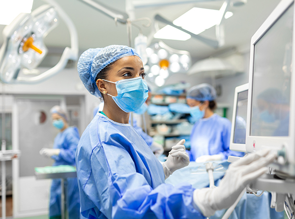 an assistant in blue scrubs operating a screen monitoring a surgery in an operating theatre